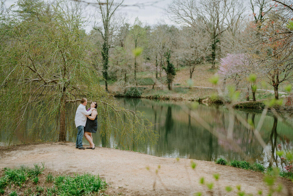 Couple holding each other and laughing on the bank of a pond. 