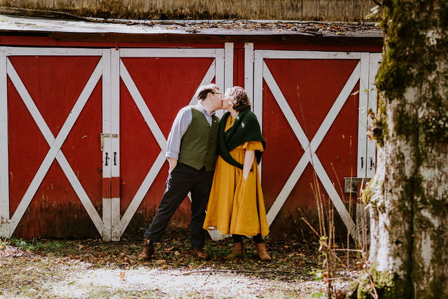 A wedding couple kissing in front of an old red barn. 