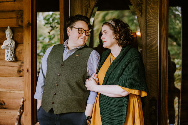 A couple at a forest elopement standing in front of a cabin smiling at each other.