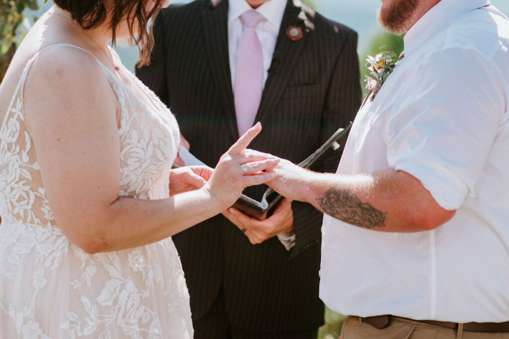 A bride slipping on a wedding band to a groom's finger. 