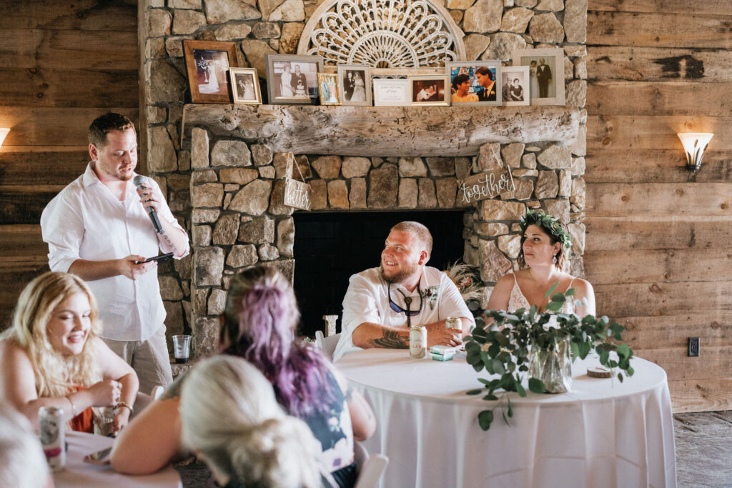 A groomsman giving a wedding toast next to the couple. 