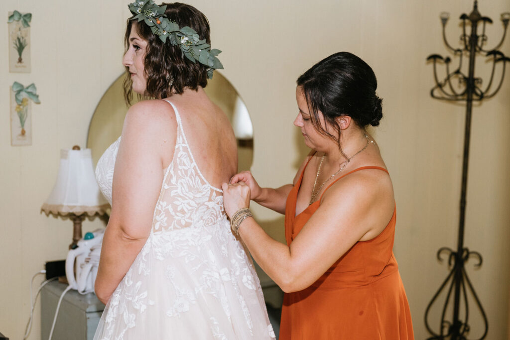 A person helping a bride zip up a wedding dress. 