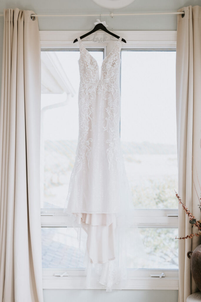 A wedding dress hanging between curtains in front of a window.