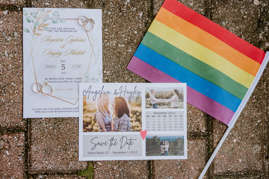 A wedding invitation, save the date, and a small pride flag laying out on a brick sidewalk. 
