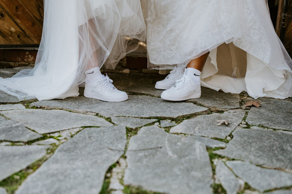 A close up view of two brides white Nike shoes under their dresses. 