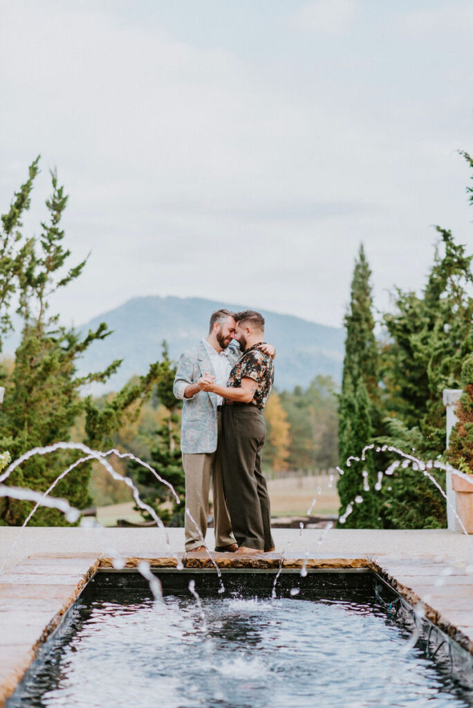 A couple holding each other close while standing on the far end of a small fountain.