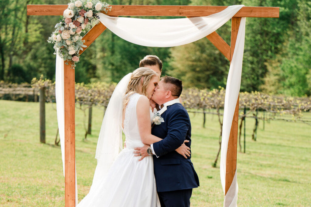 A wedding couple during their first kiss in an outdoor ceremony. 