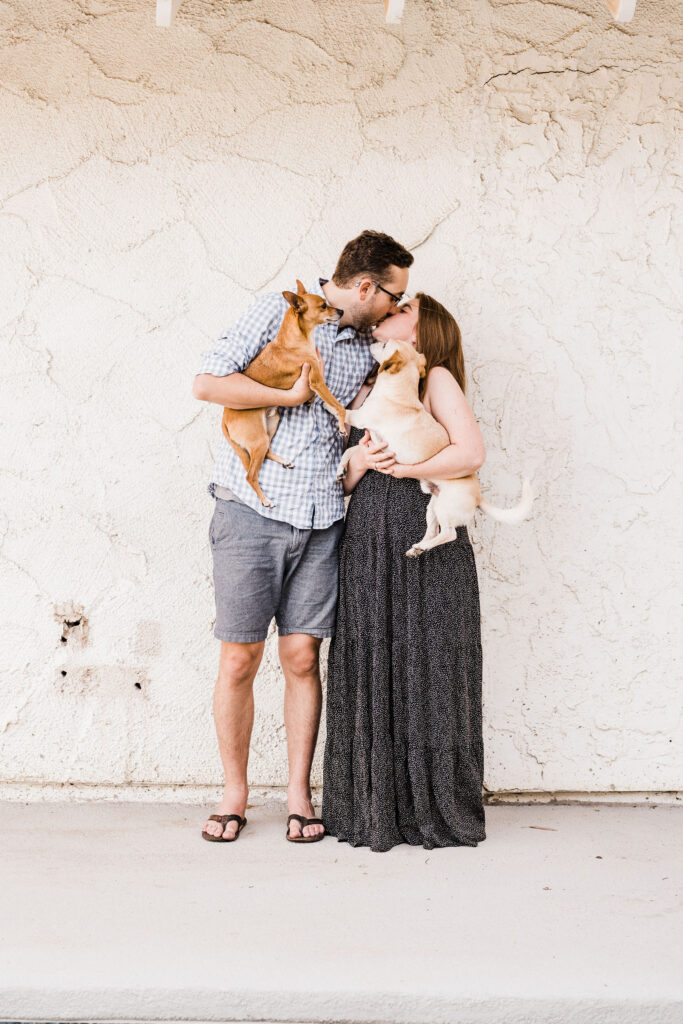 A couple kissing while both of them hold small dogs in their hands. 