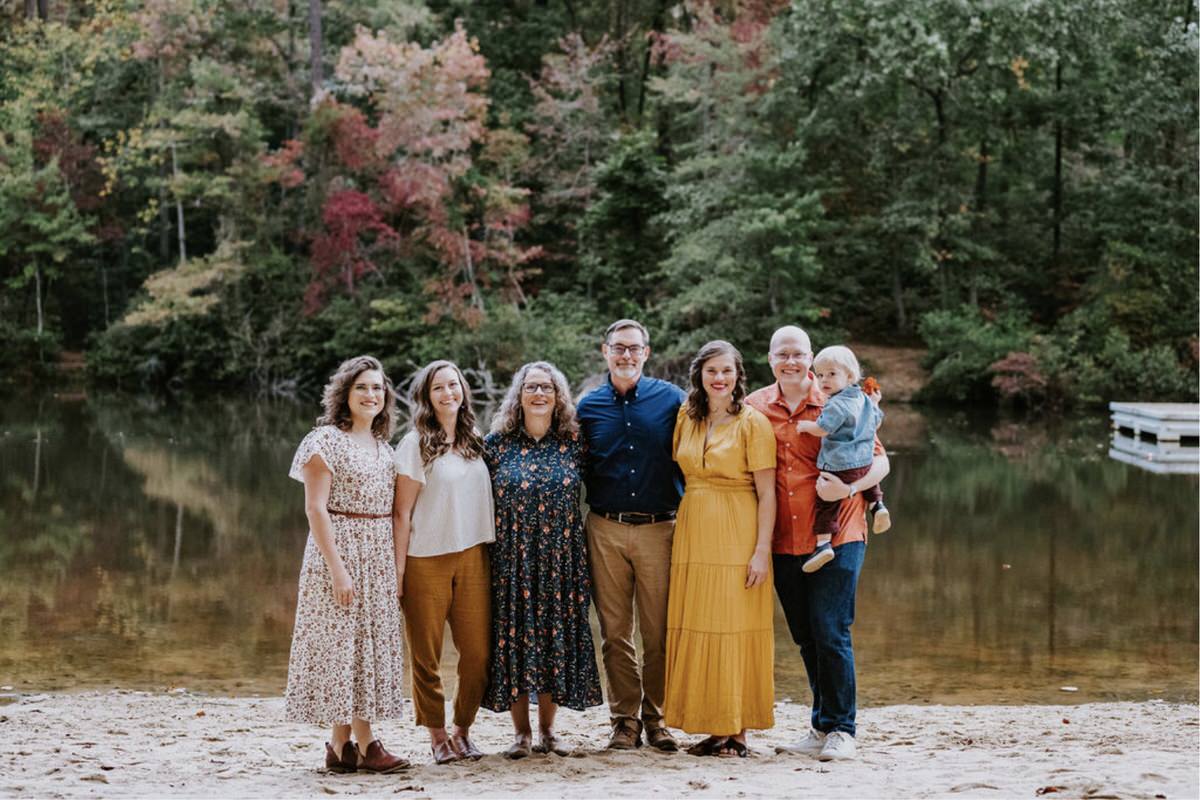 A family standing next to each other smiling in front of a small pond during an autumn family photoshoot.