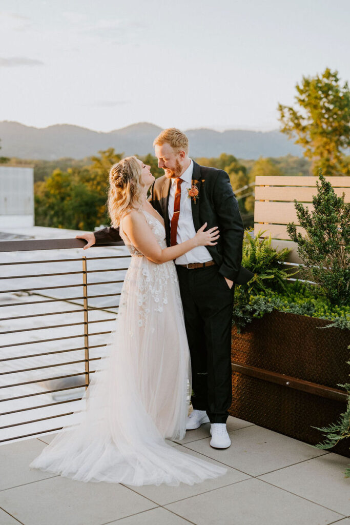 A newly married couple standing on the rooftop of the Highland Brewing Company with their arms around each other as the smile. 