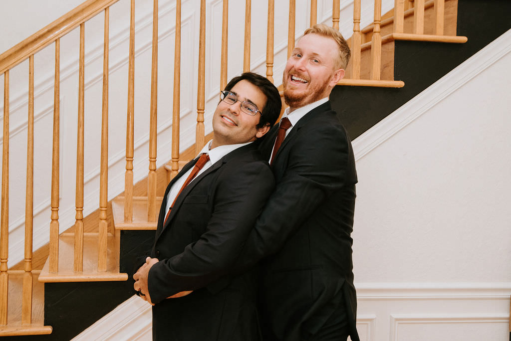 A groom standing behind his groomsmen with his arms wrapped around him like a prom picture. 