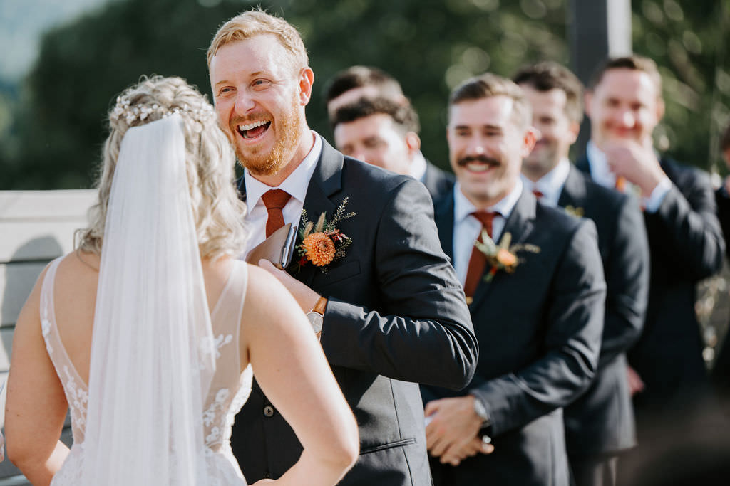 A groom laughing as he stands up with his bride during their wedding. 
