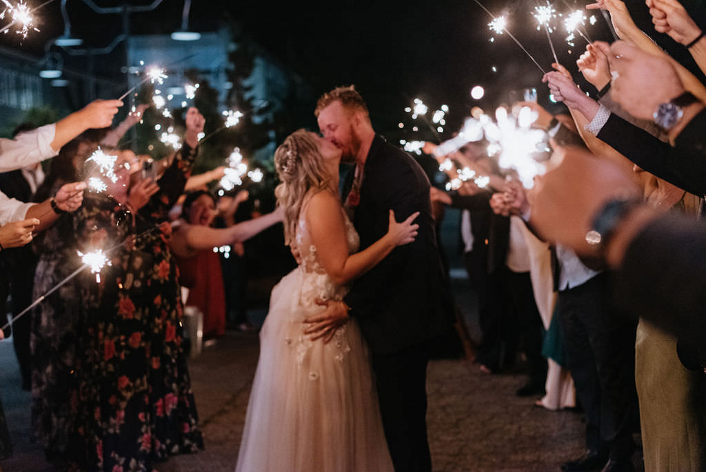 A couple kissing while standing in between their wedding guests who are holding sparklers. 