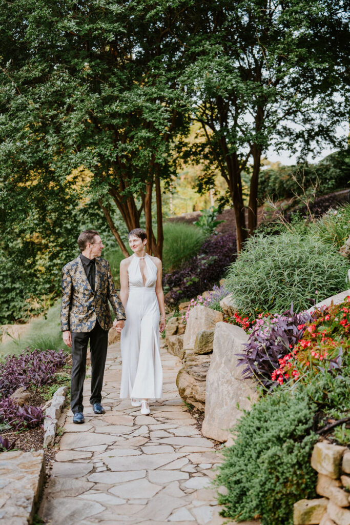 A wedding couple walking along a stone path with plants on either side.