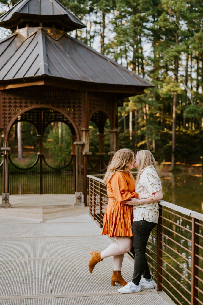 A couple kissing in front of a small gazebo on a dock. 
