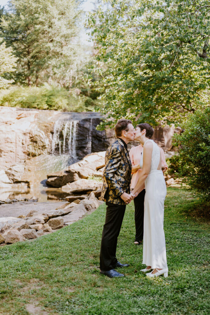 A wedding couple during their first kiss in front of a small rock waterfall. 