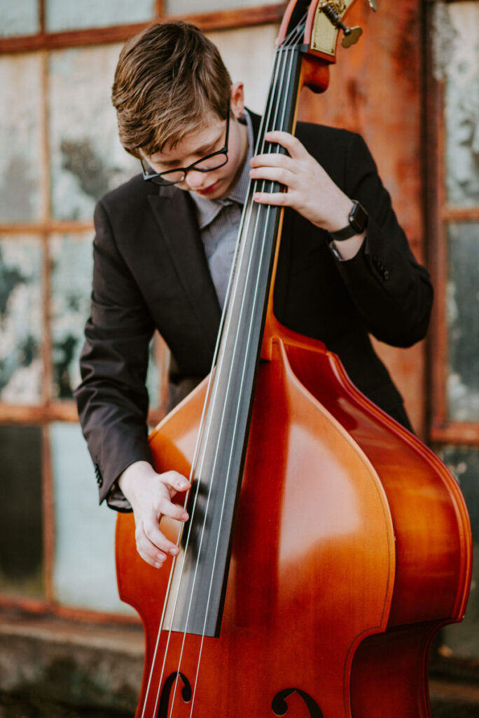 A teenager playing the cello in front of an industrial building. 
