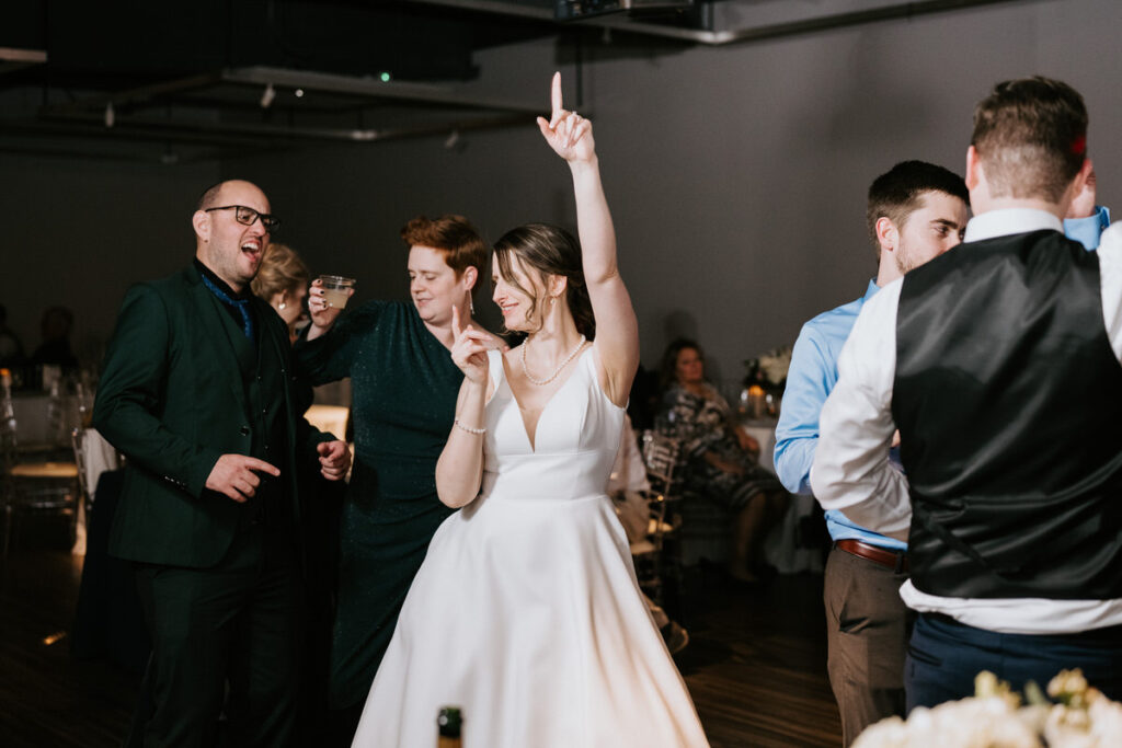 The bride and groom having a blast on the dance floor, surrounded by cheering guests, capturing the fun and excitement of a wedding reception.