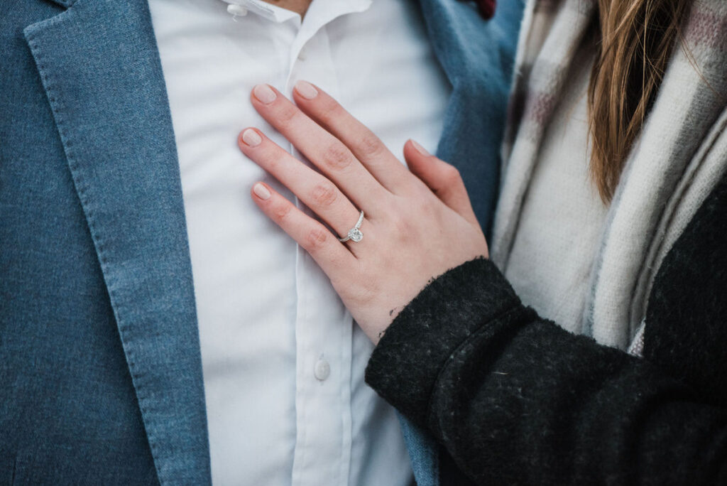 Close-up of a woman's hand with an engagement ring, resting on a man's blue blazer sleeve