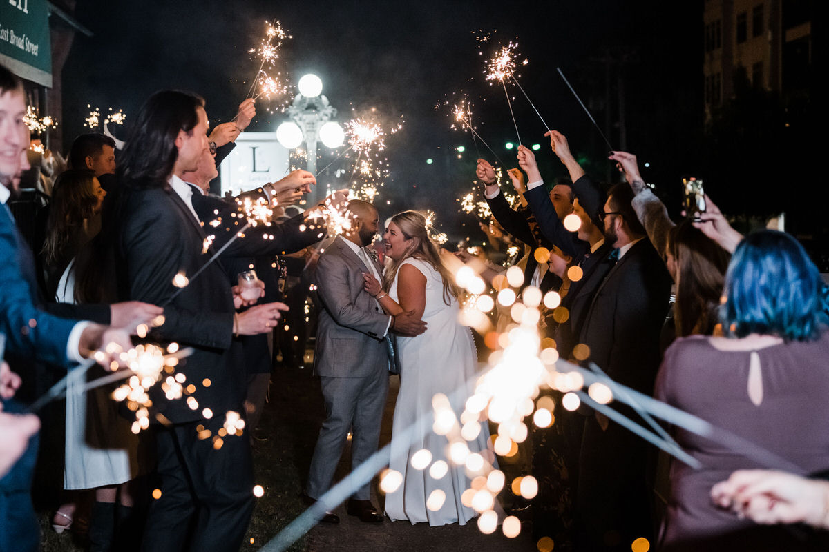 A nighttime celebration with guests holding sparklers aloft, lighting up the scene as the bride and groom share a kiss in the center