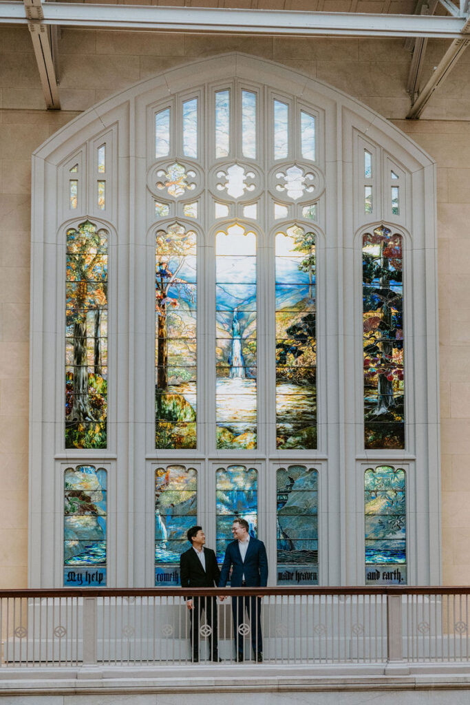 In a moment of tranquility, the two share a contemplative pause in front of a large, intricate stained glass window that bathes the space in colorful light.