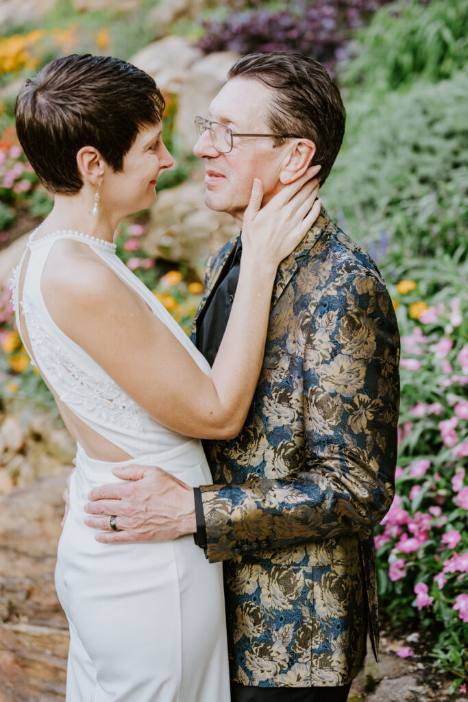 A couple holds one another surrounded by flowers.