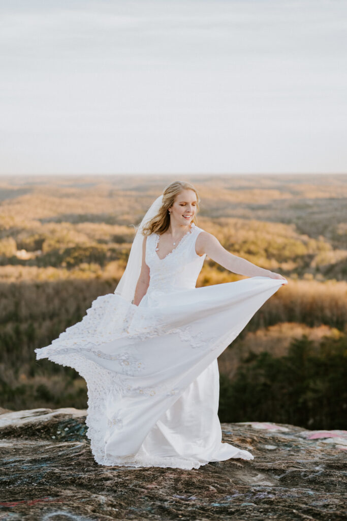 A bride twirls in a wedding dress with a fall landscape behind her.