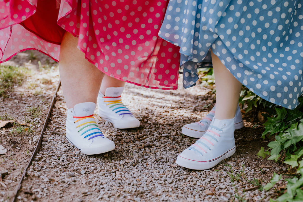 A close up of white shoes with rainbow shoelaces on them. 