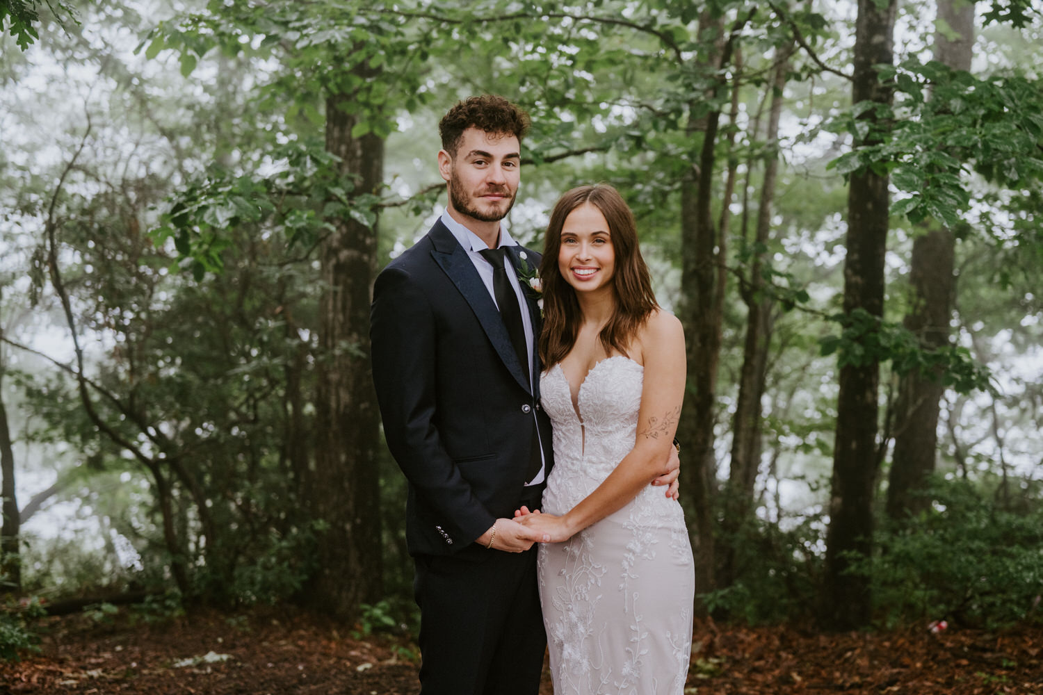 A couple poses in the forest in rainy day wedding photos.