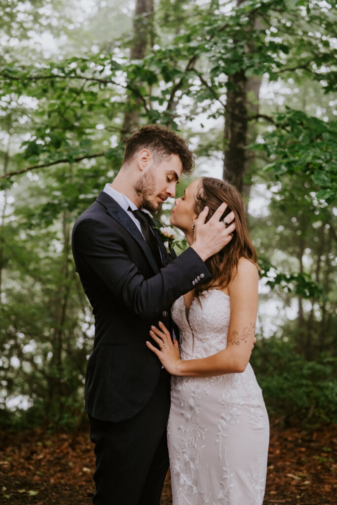 A couple leans in for a kiss in the rain in a forest.