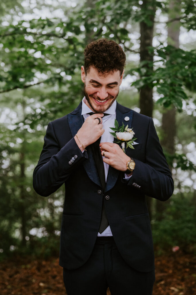 The groom fixes their tie in the forest.