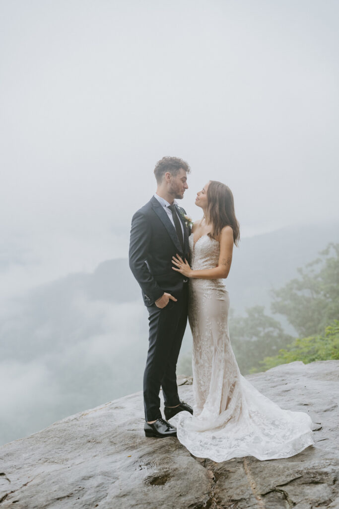 The couple looks at one another on a rock in the fog.