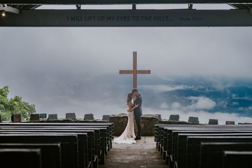 A couple holds one another in an outdoor wedding venue with mountains behind them.