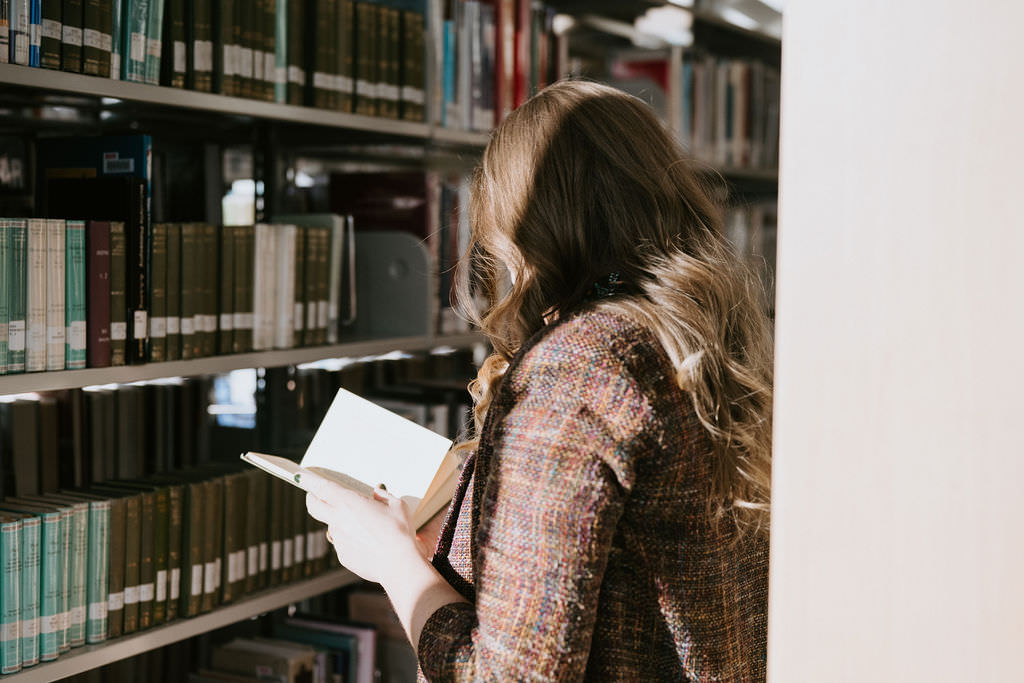 A person standing in a library looking at a book 