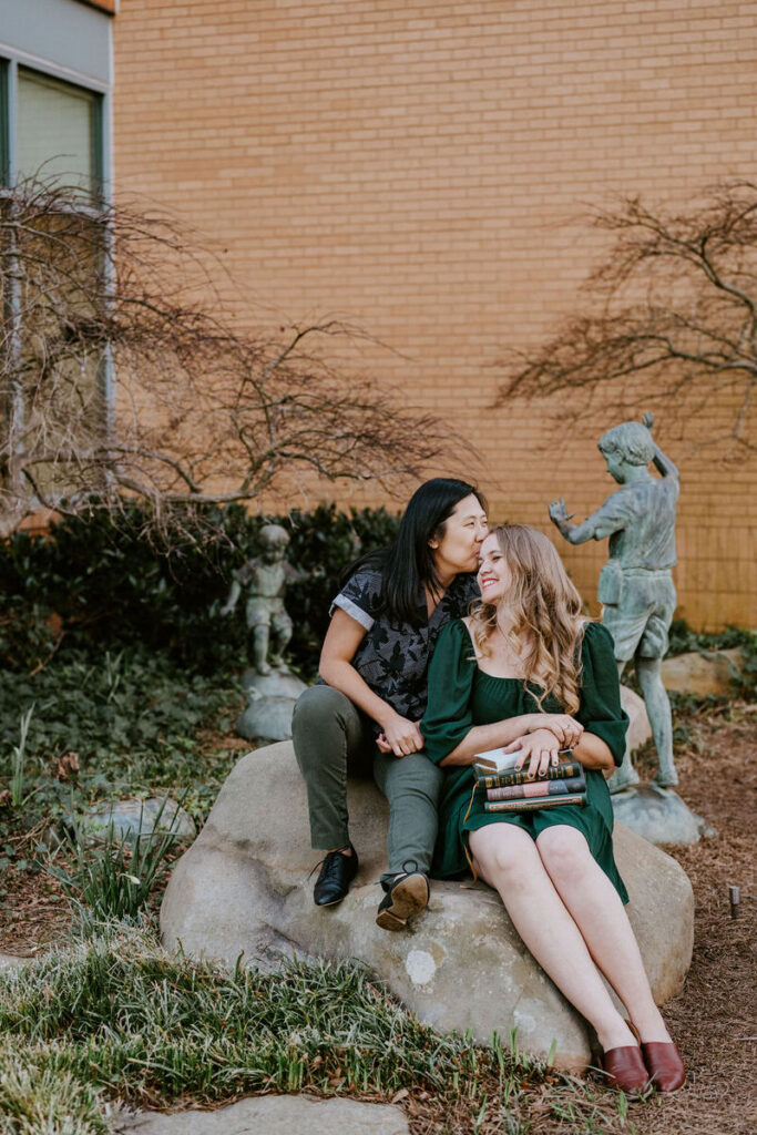 A couple sitting on a rock as one kisses the other's forehead 