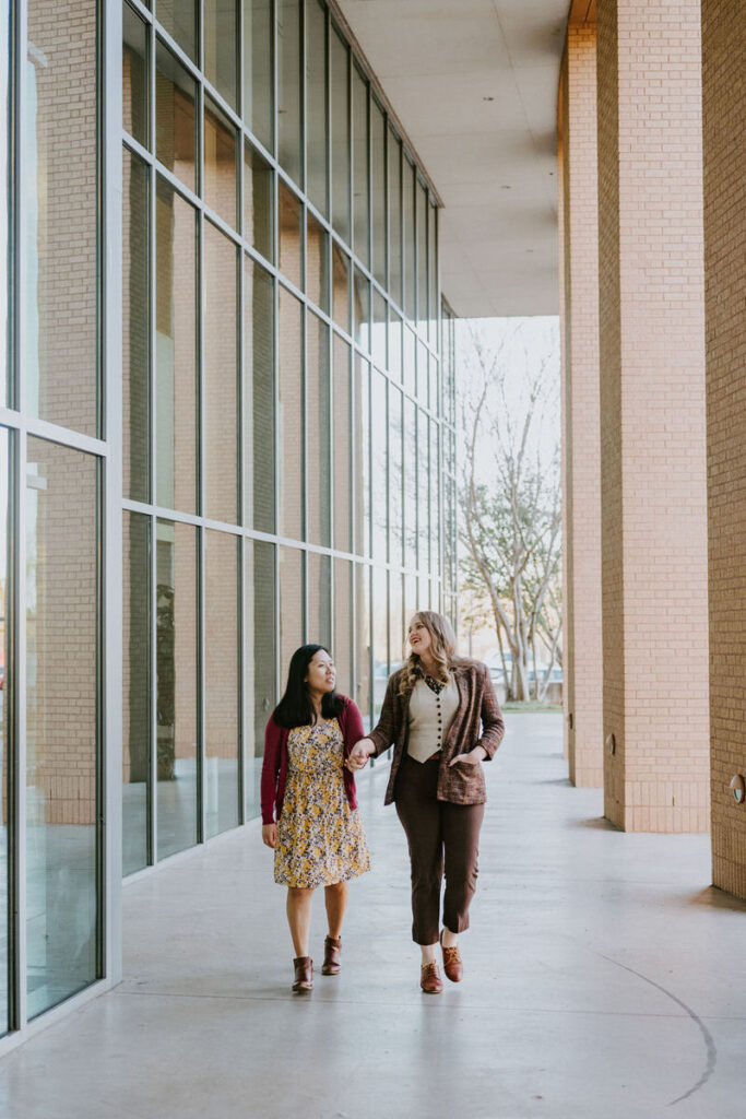 A couple holding hands and walking around the outside of a building 