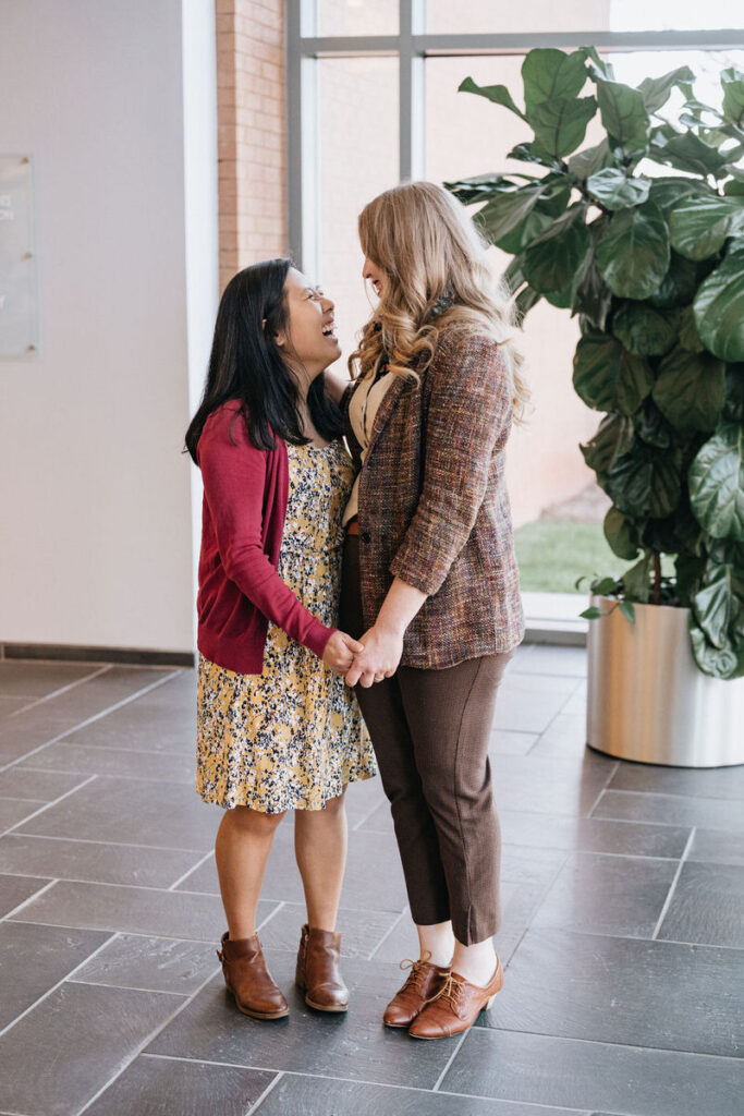 A couple holding hands and standing close as they smile at each other 