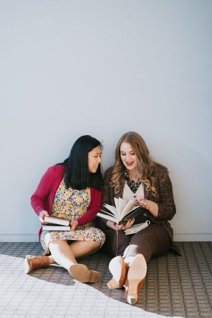 A couple sitting on the floor of a library flipping through a book 