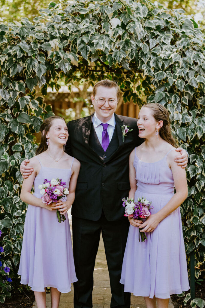 A newlywed with their arms around two younger relatives as they all smile 