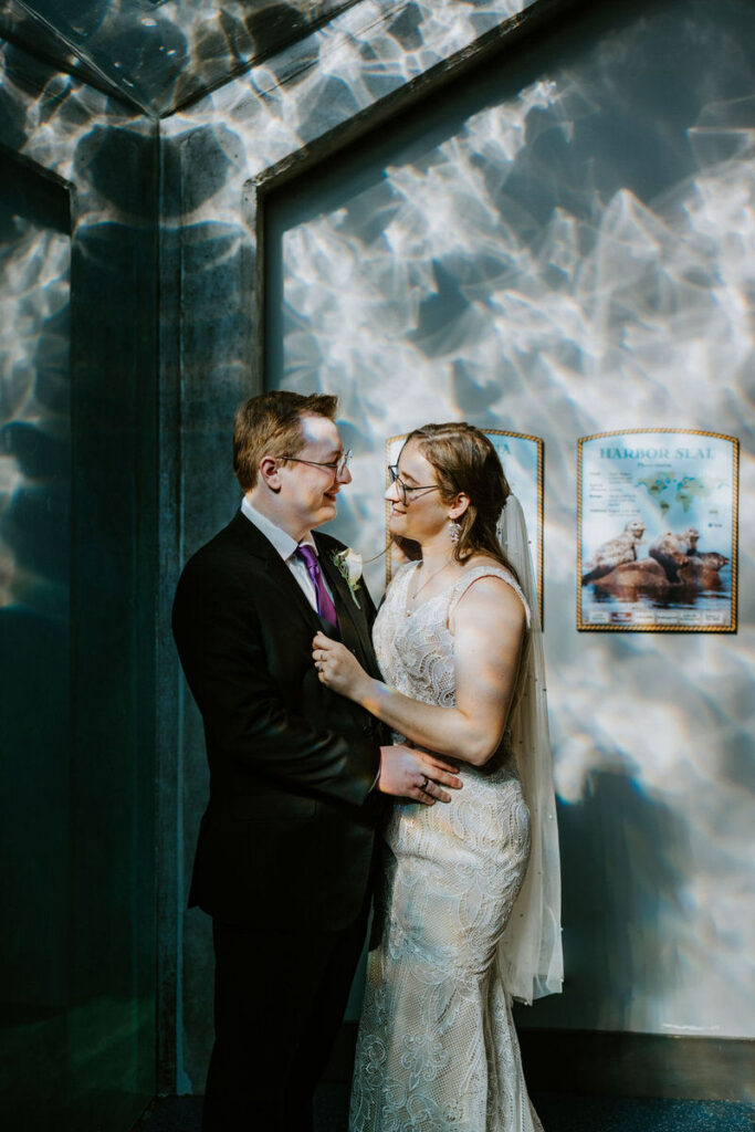 A wedding couple standing in an aquarium, with light reflecting on the walls 