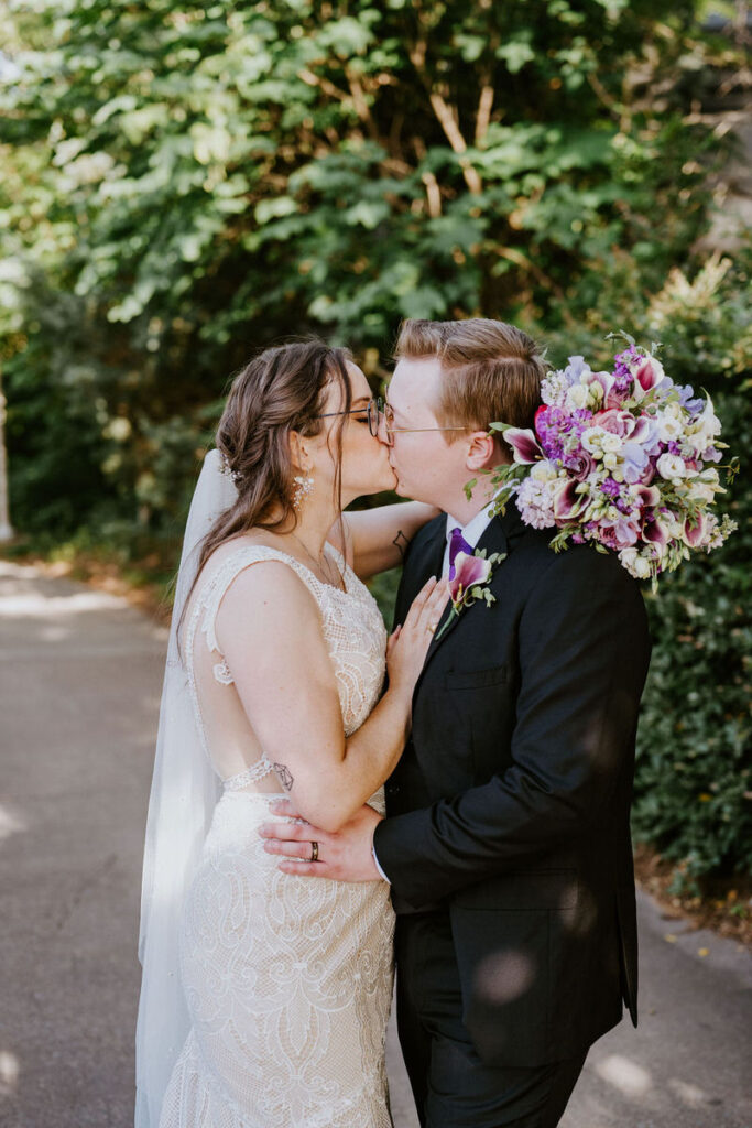 A newlywed couple kissing as one holds a bouquet of flowers 