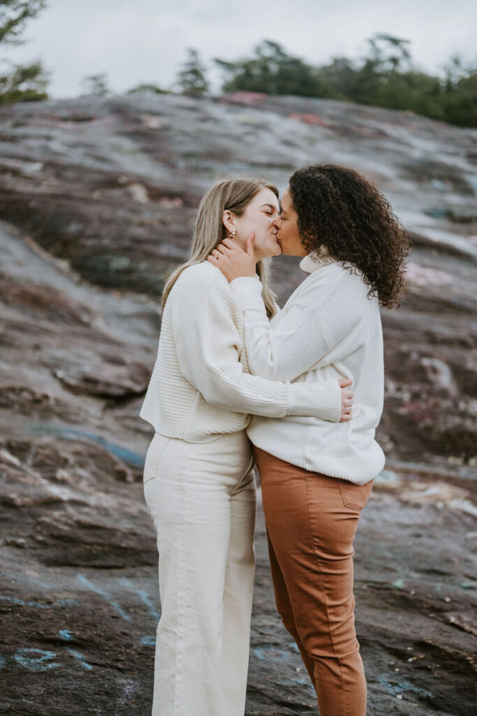 A couple kissing on a rocky mountain overlook 
