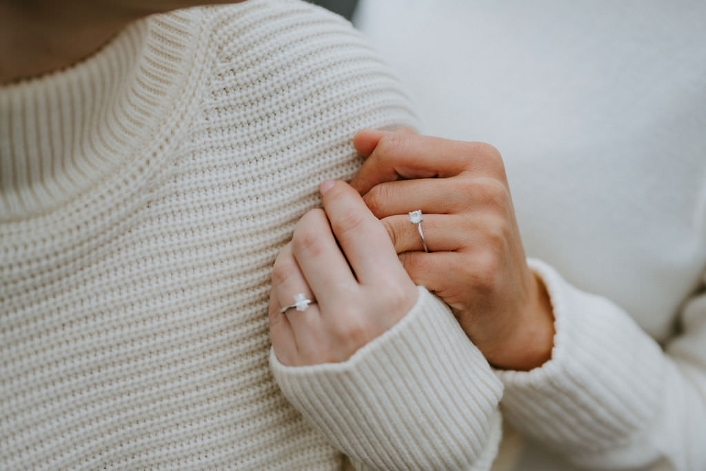 Close-up of two women holding hands, showcasing their engagement rings.
