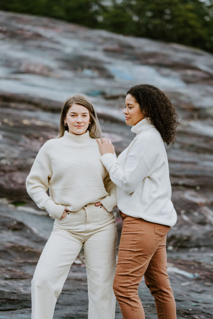 Two women standing on rocky terrain, one with her hand on the other’s shoulder