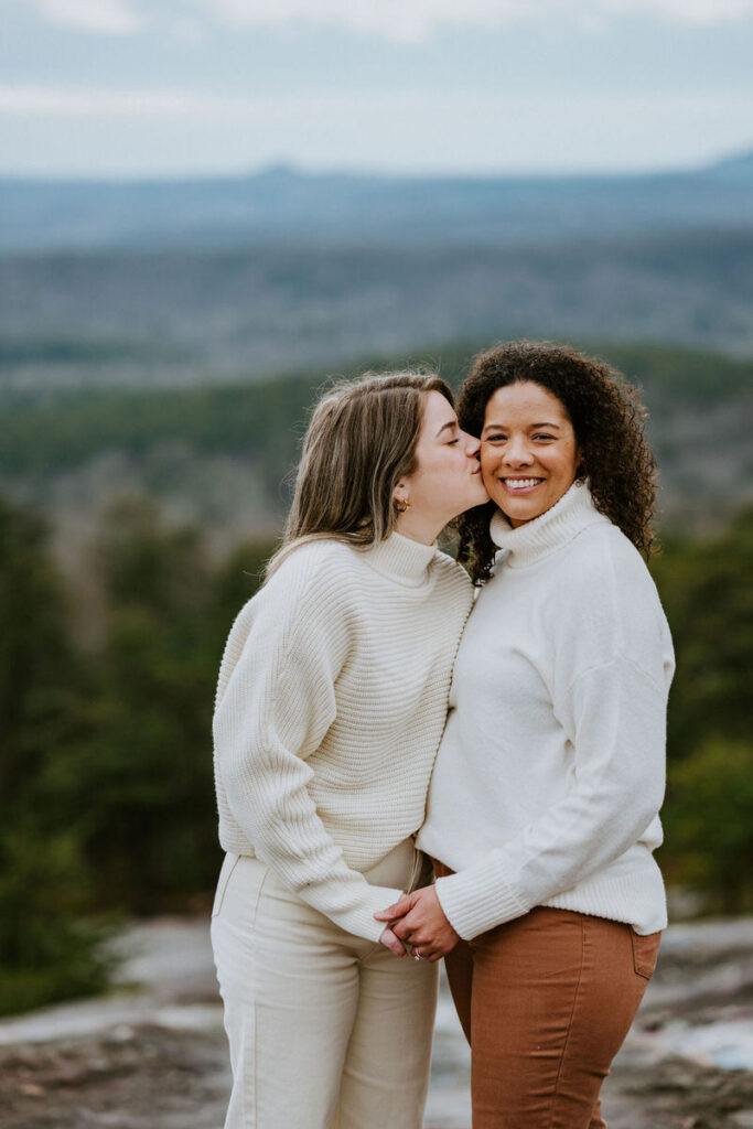 A woman kisses her partner on the cheek while they hold hands