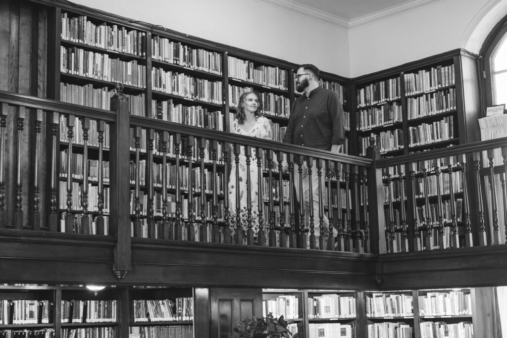 Black and white photo of a couple walking on the top level of a library smiling. 