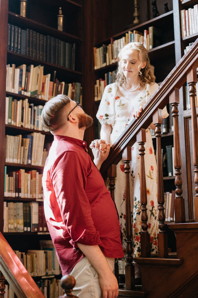 A couple standing on different levels of a staircase holding hands 
