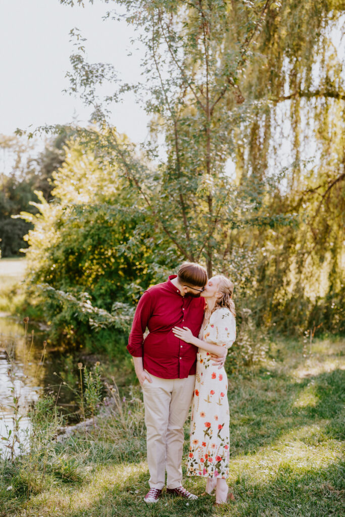 A couple kissing while standing next to a small lake. 