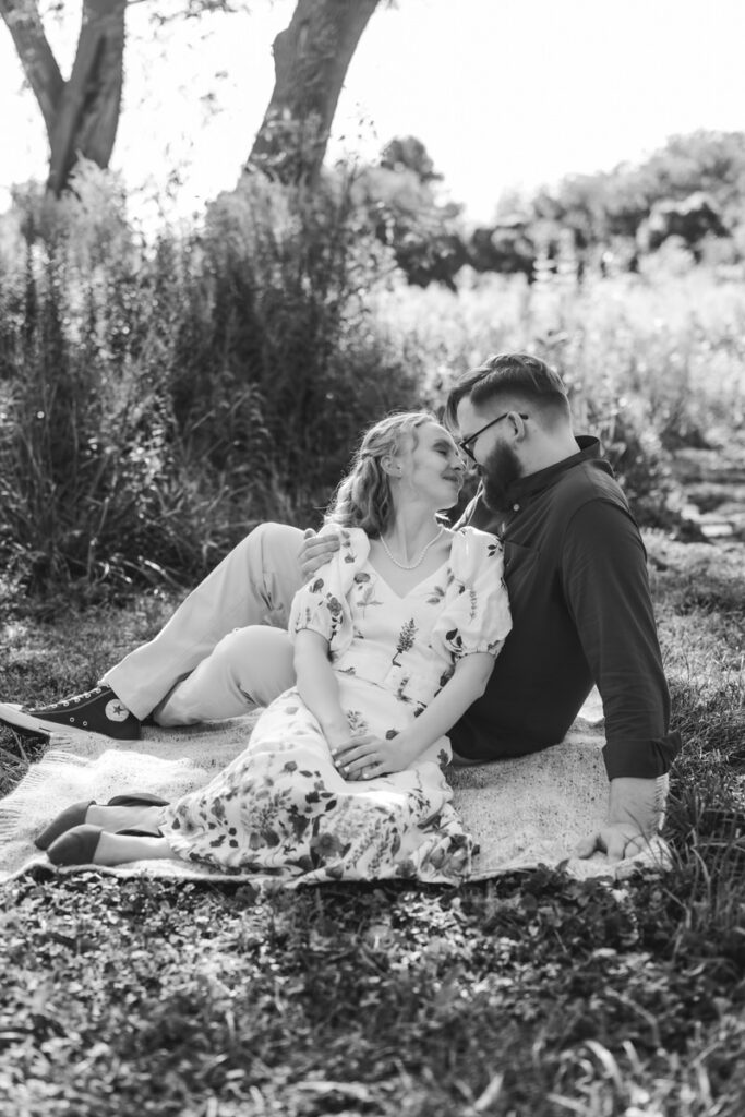 A couple sitting close together on a picnic blanket as they are about to kiss. 