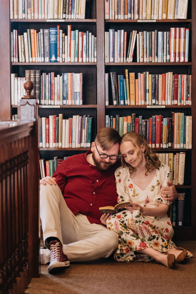 A couple sitting on the ground in a library reading a book together 